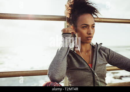 Woman athlete sitting outdoors and wearing earphones to listen music. Female listening to music during workout break. Stock Photo