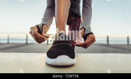 Woman tying her laces before a run. Female runner tying her shoelaces while training outdoor on a road by the sea. Stock Photo