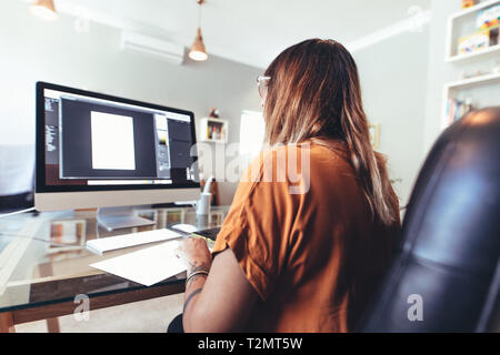 Close up of a creative artist working on computer in office. Rear view of a woman working on a computer sitting at her desk. Stock Photo