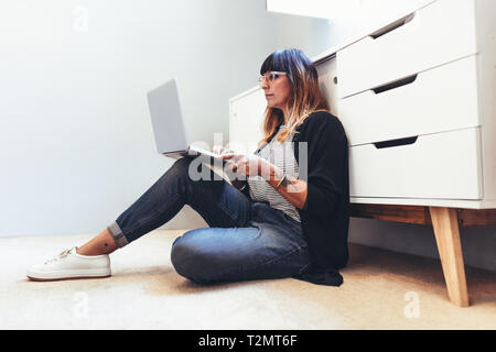 Freelance woman working on laptop computer sitting on floor. Female entrepreneur sitting down on the floor working from home. Stock Photo