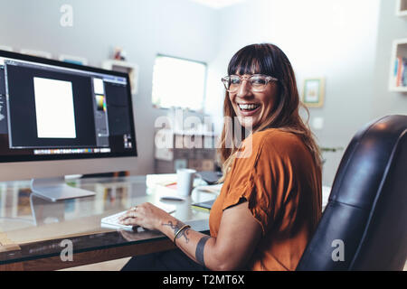 Side view of a creative artist working on her designs on a computer. Smiling artist working on digital editing in office. Stock Photo