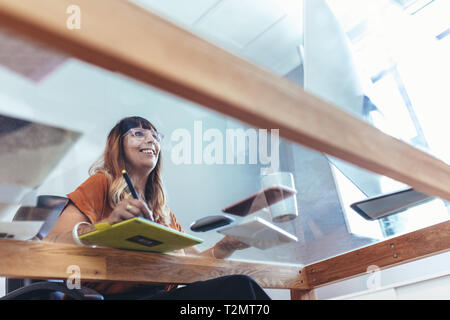 Low angle view of a female illustrator making a drawing on a digital pad looking at the computer. Smiling creative artist working on her designs on a  Stock Photo