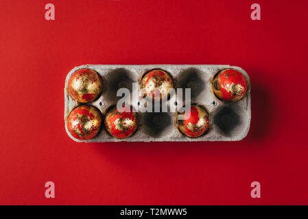 Six golden colored and decorated with sparkles Easter eggs in egg-box, Easter egg hunt celebration, colorful still life in paper box on red background Stock Photo