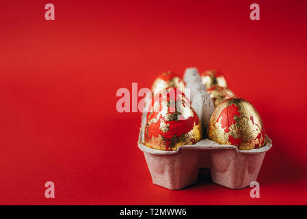 Group of golden colored and decorated with sparkles Easter eggs. Easter egg hunt celebration, colorful still life in paper box on red background. Stock Photo