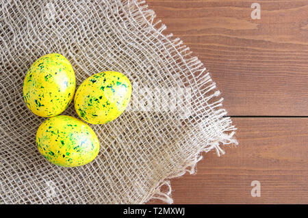 Easter eggs of yellow color with green splashes. On linen fabric brown. Wooden brown background. Stock Photo