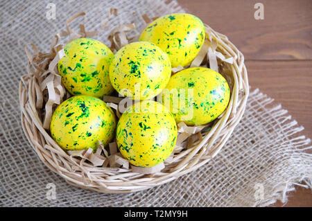 Yellow Easter eggs in a basket. On linen fabric brown. Wooden brown background. Stock Photo