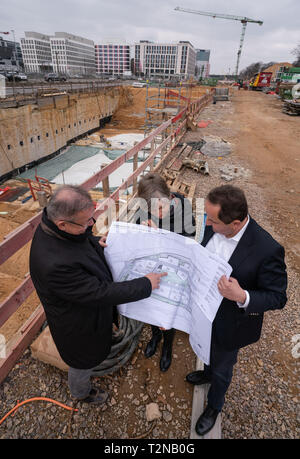 26 March 2019, Hessen, Frankfurt/Main: The two managing directors of Gateway Gardens, Manfred Dittrich (l) and Jörg Guderian (r), stand together with Carolyn von Monschow (M), managing director of Gateway Gardens Projektentwicklungs GmbH, and a plan in front of one of the numerous construction sites on the grounds of Gateway Gardens. On the site of the former US Airbase, a new city district is being built with offices, hotels, restaurants, shopping facilities, medical facilities and a day care center for children. Up to 18,000 people could work there once in the future, and more than 200 subur Stock Photo