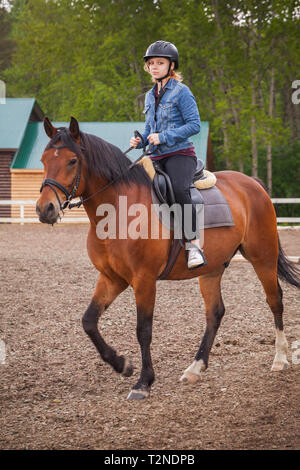 Beginner riding lessons, teenage girl rides brown horse on riding field, vertical photo Stock Photo