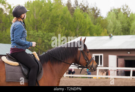 Teenage girl rides brown horse on riding field, close-up profile photo Stock Photo