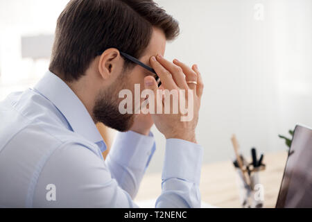 Stressed businessman with eyewglasses touching head working at office. Worker feels eyes fatigue and headache close up view over the shoulder. Influen Stock Photo