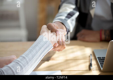 People sitting at the desk in office. Close up handshake two successful business people after good deal, broker and client shaking hands after sales n Stock Photo