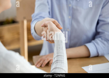 People sitting at the desk in office. Close up handshake two successful business people after good deal, broker and client shaking hands after sales n Stock Photo
