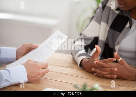 Close up people hands on a wooden table, boss and candidate woman during interview. Director hr manager holding resume paper, african woman talking ab Stock Photo