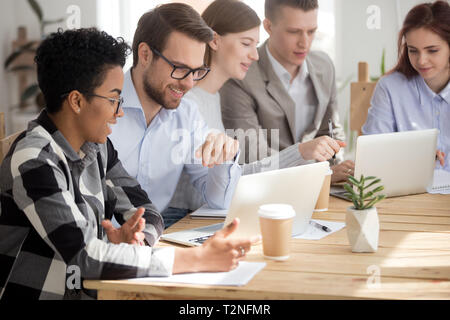 Diversity colleagues sitting together at the desk in office boardroom using computers, have a break talking. Positive friendly multiracial people at w Stock Photo