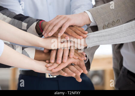 Close up of multiracial group of millennial business people or students standing stacking theirs hands palm together. Gesture sign of support unity an Stock Photo