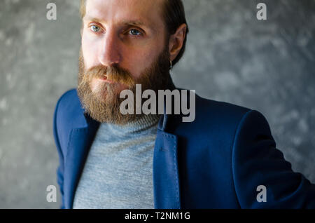 Fashion Portrait of Bearded Man with an Indifferent Haughty Look in Gray High Neck Sweater on Gray Background. Stock Photo