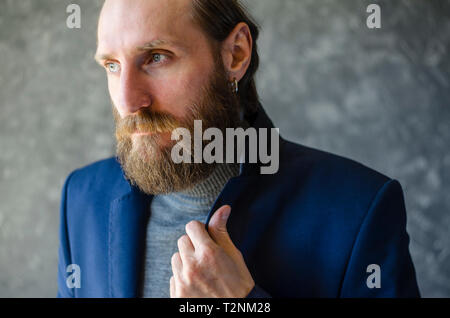 Fashion Portrait of Bearded Man in Gray High Neck Sweater Adjusting Collar in Blue Suit Blazer. Stock Photo