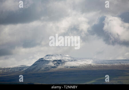 Ingleborough mountain with a covering of snow under clouds on April 2 2019. Ingleborough is popular with hill walkers and forms part of the Three Peak Stock Photo