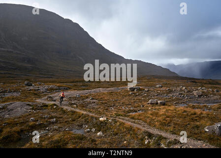 Male mountain biker biking on dirt track in mountain valley landscape, rear view,  Achnasheen, Scottish Highlands, Scotland