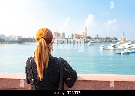 Female tourist with red hair looking out over sea toward Montaza palace, rear view, Alexandria, Egypt Stock Photo