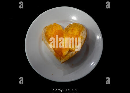 hearth shaped bread with jam marmalade on white plate isolated on black Stock Photo