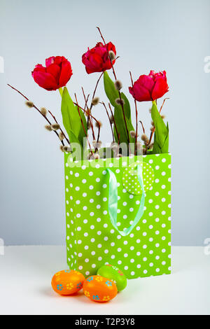 Tulips and willow in a shopping bag and Easter eggs on a light background.  Easter greeting card. Stock Photo