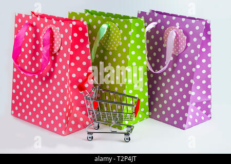 Three multi-colored shopping bags and shopping car on a light background. Stock Photo
