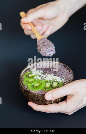 Healthy smoothie with fruits, plate made from coconut shell and wood spoon. Kiwi, banana, black currant Stock Photo