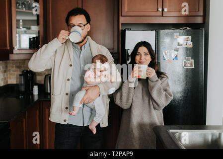 Couple having drink and carrying baby daughter in kitchen Stock Photo