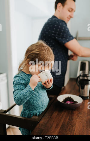 Female toddler with father drinking from cup at kitchen counter Stock Photo