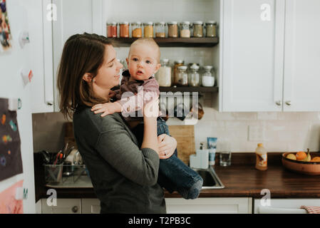 Mother carrying baby son in kitchen Stock Photo