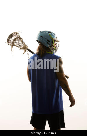 Young male lacrosse player carrying lacrosse stick on his shoulder, rear view against white background Stock Photo