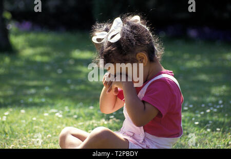 little girl sitting in garden rubbing her eyes Stock Photo