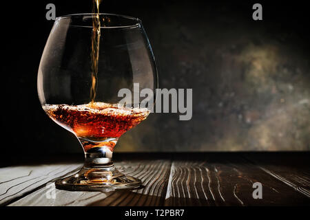 Cognac is poured into a glass on an old dark wooden background. Free copy space. Selective focus. Horizontal. Stock Photo