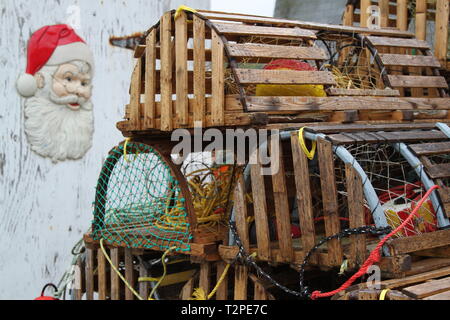 Stack of traditional wooden lobster traps in Newfoundland with plastic Santa Claus head on wall Stock Photo