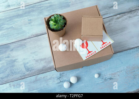 Two carton boxes and one pot with green plant and fragile signs on a blue wooden surface Selective focus Stock Photo