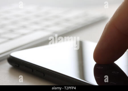 Smartphone with finger touching the screen and keybord in background. Selective focus and extreme close up and hard contrast fading out for copy writi Stock Photo