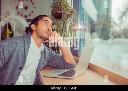 Pensive young man in front of the laptop looking up to side thoughtful daydreaming. Closeup portrait of a handsome guy wearing white shirt, gray blous Stock Photo