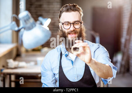 Happy bearded man working with ceramic workpieces at the working place of the pottery shop Stock Photo
