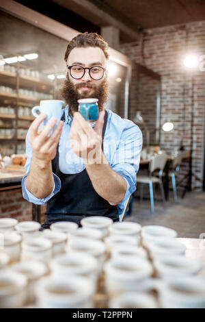 Portrait of a creative bearded potter man holding ceramic products at the pottery shop Stock Photo