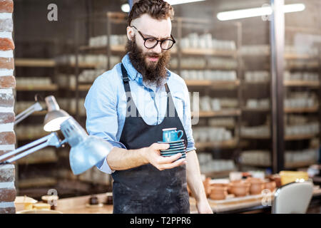 Portrait of a creative bearded potter man or business owner holding ceramic products at the pottery shop Stock Photo