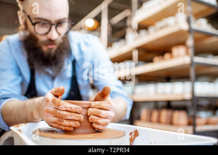 Handsome man as a potter worker in apron making clay jugs on the pottery wheel at the small manufacturing Stock Photo
