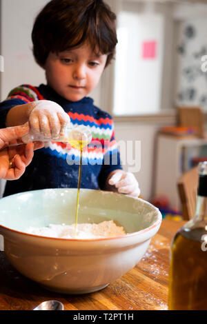 Toddler helping mother pour oil into flour in mixing bowl Stock Photo