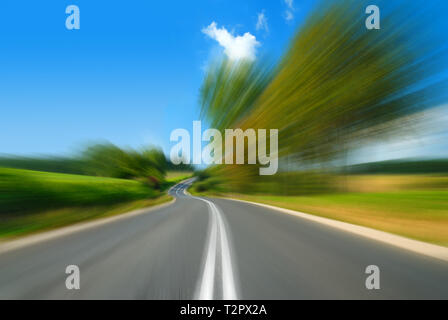Road among green fields with motion blur effect, blue sky in the background Stock Photo