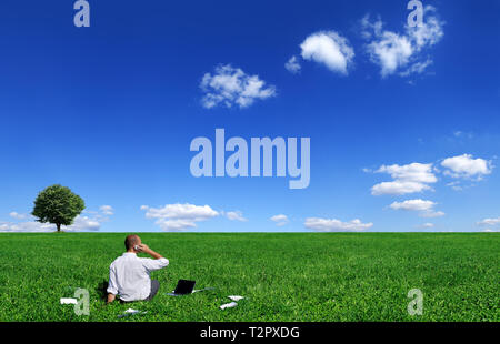 Businessman sitting on green field, blue sky and white clouds in background Stock Photo