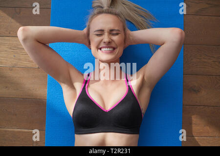 Fitness determined middle aged woman lying doing crunches at home on gym mat. She lying on the floor in the living room. View from above. Stock Photo
