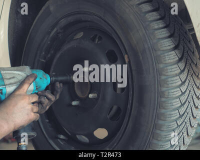 Mechanic changing a car tire in a workshop on a vehicle on a hoist using an electric drill to loosen the bolts in a concept of service or replacement Stock Photo