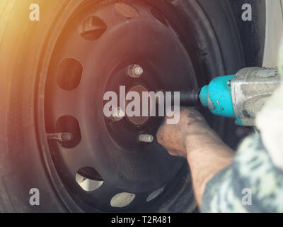 Mechanic changing a car tire in a workshop on a vehicle on a hoist using an electric drill to loosen the bolts in a concept of service or replacement Stock Photo