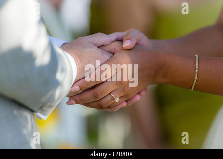 Bride and groom holding hands after a wedding ceremony. Intermarriage - Caucasian man and Asian woman. Stock Photo