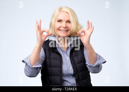 Smiling senior blonde lady gesturing perfect ok sign. Positive human facial emotion Stock Photo